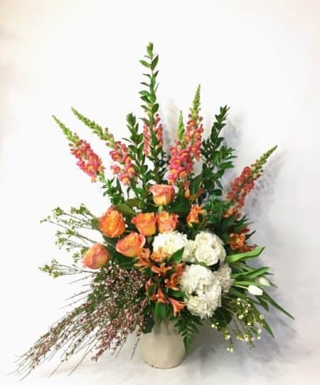 Large orange arrangement in a beautiful ceramic container. Full of Snapdragons, Hydrangea, Tulips, Roses, Spray Roses, Alstroemeria, Genista and gorgeous greens.