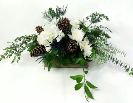 Gorgeous white flowers with hints of blue are paired with natural accents in a wooden container perfect for a cozy holiday table.